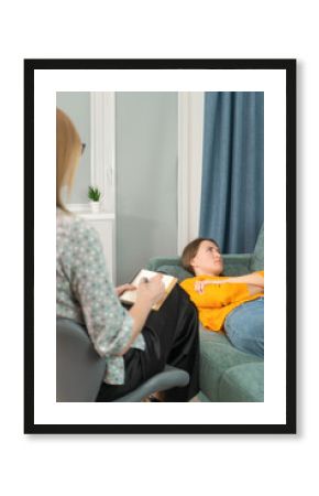 Young woman lying and resting on the couch with a psychologist sitting next to her and supporting her during psychological therapy. Relaxation during a session with a psychotherapist. Psychosomatics.