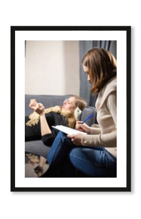 Concentrated specialist writes in notepad listening to client. Woman lies on couch sharing negative stories and feelings with psychologist