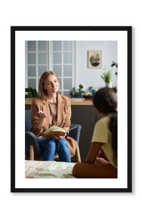 Vertical image of psychologist talking to problem child and making notes in notebook