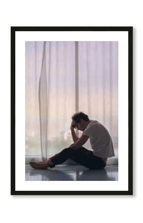 Depressed caucasian man losing job and heartbroken at same time sitting alone near window in dark at evening time with low light environment, PTSD Mental health and depression concept.