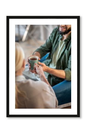 Man smiling while taking cup of tea from psychologist