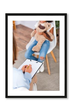 Cropped view of psychologist writing on clipboard during consultation with blurred african american girl on background