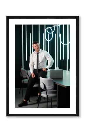 Businessman wearing modern suit and stands in contemporary office. Young specialist with a good figure and stylish suit stands leaning on the table in the kofverenz hall.