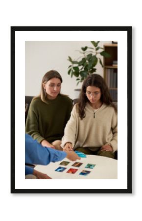 Vertical portrait of teenage girl choosing metaphorical cards handed by therapist during counseling session with mother, interactive psychology exercise