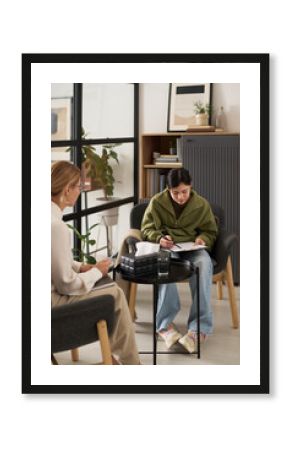 Vertical full length portrait of teenage girl filling in assessment test form during therapy session with female psychologist