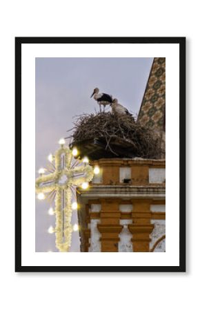 Cross illuminated with bulbs above stork nests in Carrion, Seville