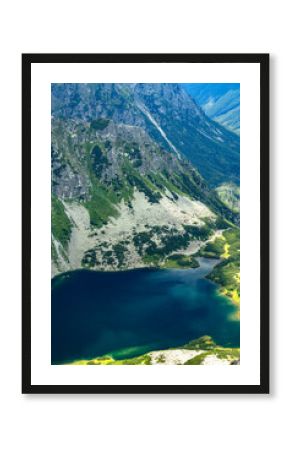 Deep blue lake at the base of steep rocky mountain slopes with green patches