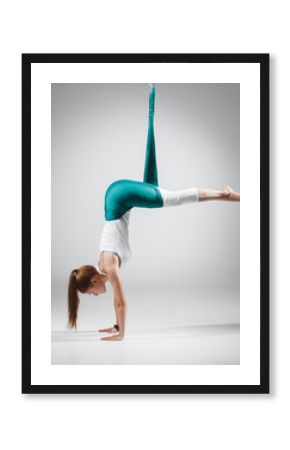 Young woman practices different inversion aerial yoga with a hammock in a white studio. Concept of a mental and physical health and harmony living