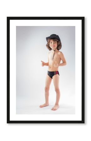 Little curly-haired cowboy hat and bathing suit standing and looking at the camera. Gray background.