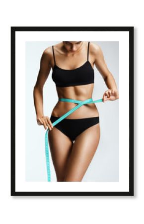 Slim girl in black lingerie with a ribbon measures the size of the waist. Beautiful part of female body. Fitness or body care concept