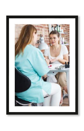 Woman polishing nails to unhappy female client  in modern beauty salon