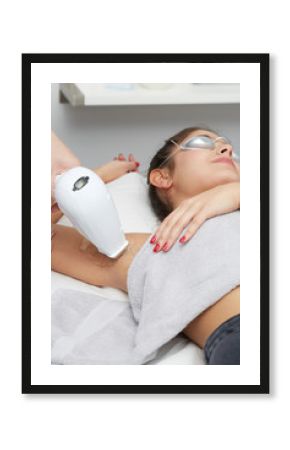 Young woman having underarm laser hair removal treatment in salon