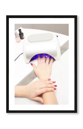 closeup of a uv lamp with a female hand inside fixing the gel nail polish at the beauty salon