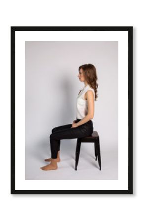 girl in white jacket and black pants barefoot sitting on chair sideways