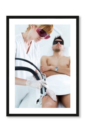 Young beautician removing legs hair with a laser to her client in the beauty salon.