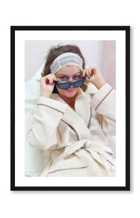 Young woman in bathrobe and with protective glasses for laser hair removal
