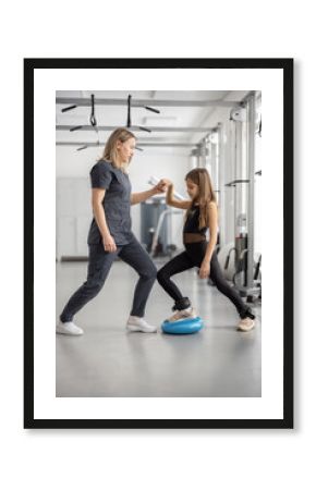 Rehabilitation specialist helping little girl to do exercises at gym. Concept of physical therapy for back health and correct posture for kids