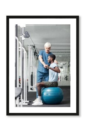 Full length portrait of physiotherapy specialist helping African American young man doing rehabilitation exercises in gym, copy space