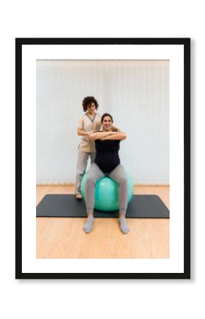 A pregnant woman doing exercises sitting on a fitness ball with her arms in front with the help of physiotherapist