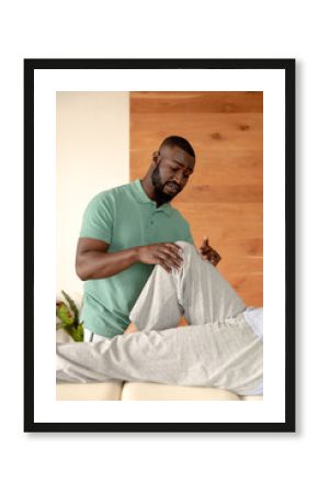 African american male physiotherapist giving leg massage therapy to caucasian senior woman at home