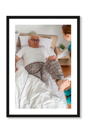 Nurse kinesiologist physiotherapist stretching, and masseuring leg of elderly man at his home. Solicitous professional medical female staff caring for senior patient. Lifestyle, nursing service