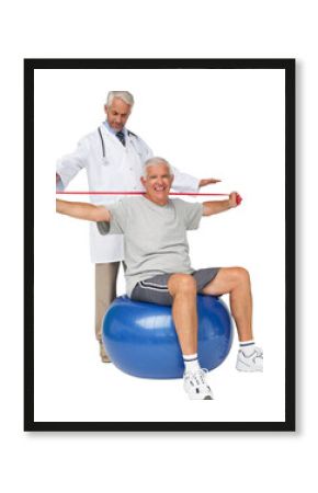 Mhysiotherapist looking at senior man sit on exercise ball with yoga belt