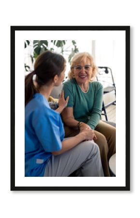 Happy satisfied senior woman holding hands with nurse, enjoying her company and kindness. Lovely elderly woman talking to healthcare specialist during home visit. Home care for people in retirement.