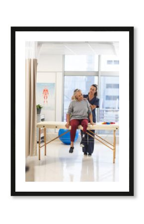 Caucasian female physiotherapist and senior woman with artificial leg massaging back at hospital