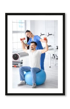 Young man training with dumbbells and physiotherapist in rehabilitation center