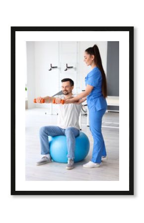 Young man training with dumbbells and physiotherapist in rehabilitation center