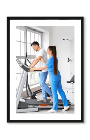 Female physiotherapist working with young man on treadmill in rehabilitation center