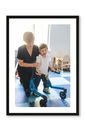 Cute young boy with cerebral palsy enjoys a session of physical rehabilitation, supported by a therapist using rehab walker in light-filled space