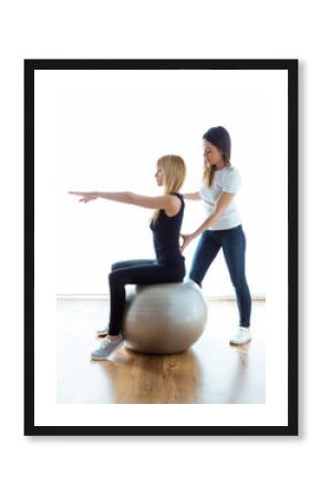 Physiotherapist helping patient to do exercise on fitness ball in physio room.