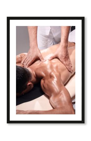 two young man, 20-29 years old, sports physiotherapy indoors in studio, photo shoot. Physiotherapist massaging muscular patient back side of shoulder or arm, with his hands close-up.