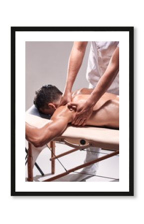 side view, two young man, 20-29 years old, sports physiotherapy indoors in studio, photo shoot. Physiotherapist massaging patient shoulder with his hands.