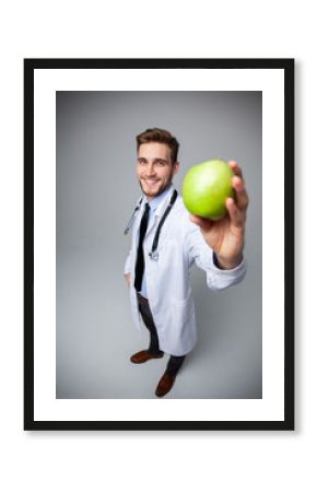 Portrait of handsome doctor in white coat looking at camera and smiling while holding an apple, isolated on white.