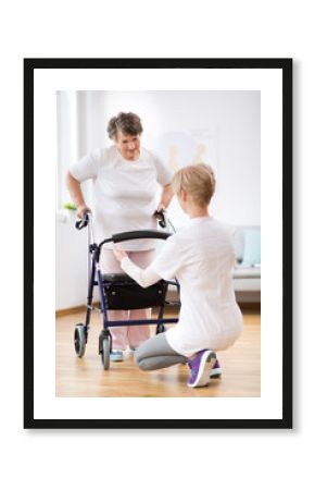 Senior woman with walker trying to walk again and helpful physiotherapist supporting her