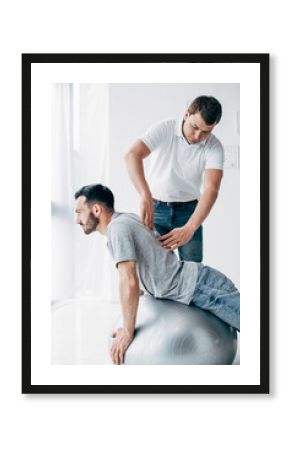 chiropractor massaging back of handsome man lying on fitness ball