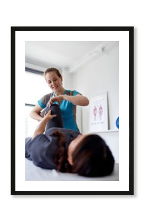 Caucasian woman physiotherapist strectching the leg and knee of a mid-adult chinese female patient sitting on a massage table