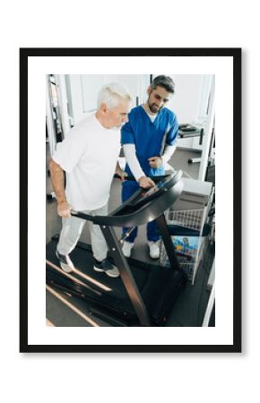 Elderly man doing cardio workout on a treadmill, therapist helping senior patient to recovery