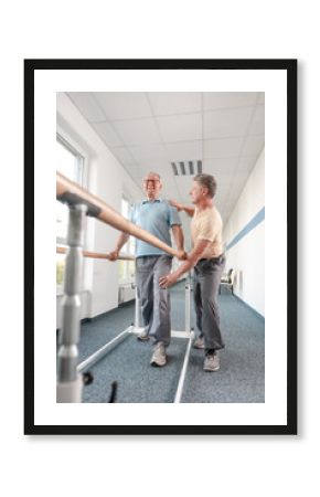 Physiotherapist helping senior man in rehabilitation walking on the bars