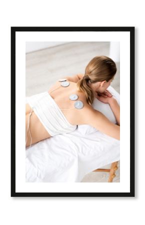 Back view of woman with electrodes on back on massage couch during electrode treatment