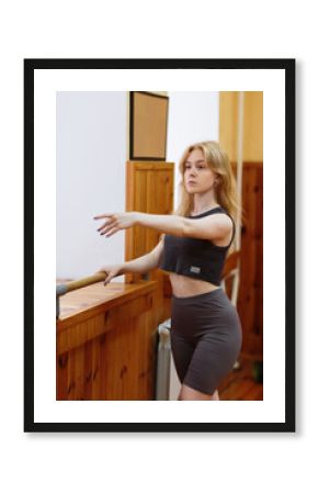 A young woman in a dance studio performing ballet exercises at the barre, improving posture and confidence