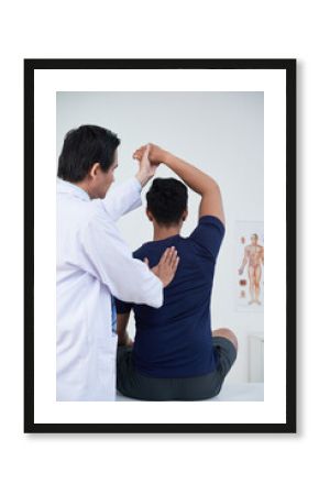 Vertical medium back view shot of modern mature osteopathic therapist treating young man manipulating his bones, muscles and fasciae