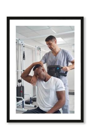 Focused male physiotherapist carrying out percussive therapy