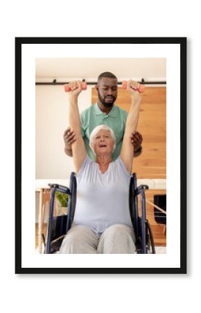 African american male physiotherapist helping caucasian senior woman to do exercise with dumbbells