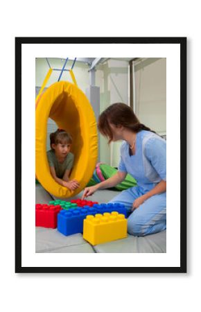 Child girl in roller tonnel during sensory integration session. child with physiotherapist in rehabilitation centre. neuro corrections children