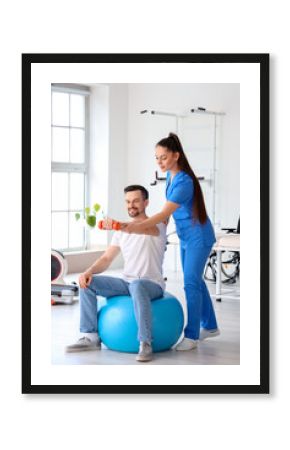 Young man training with dumbbell and physiotherapist in rehabilitation center