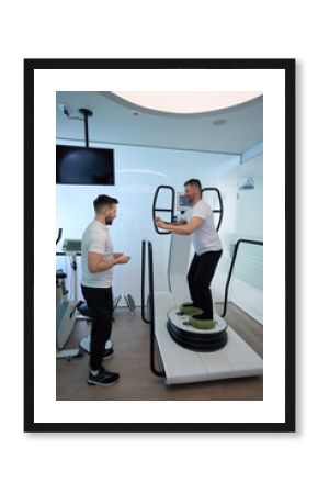 Patient working out on modern rehab equipment supervised by physiotherapist