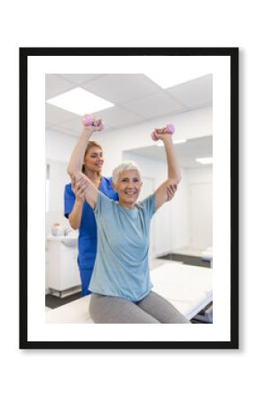 Oder aged woman doing physiotherapy with support from physiotherapists . Senior elderly female sitting in clinic using dumbbells workout exercise for patient with caregiver in nursing care.